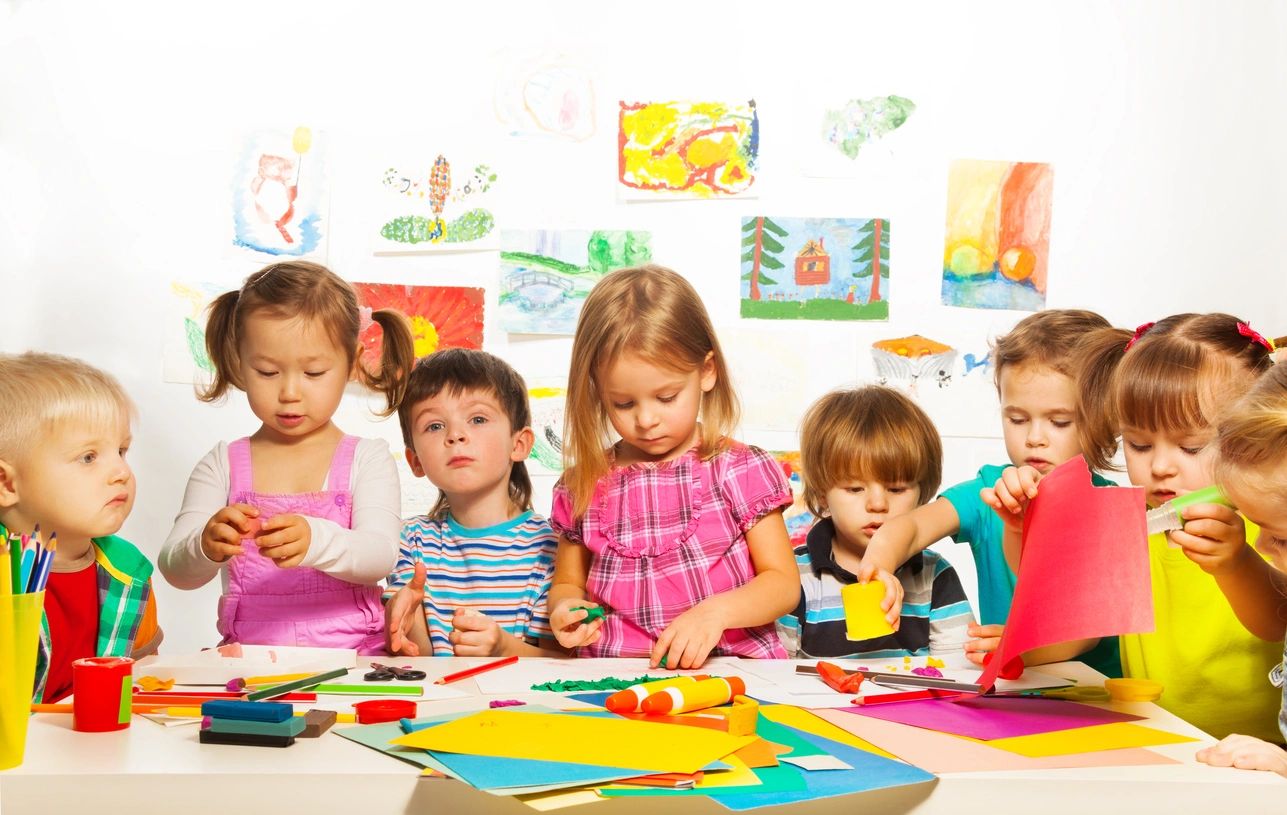 A group of children sitting at a table with art supplies.