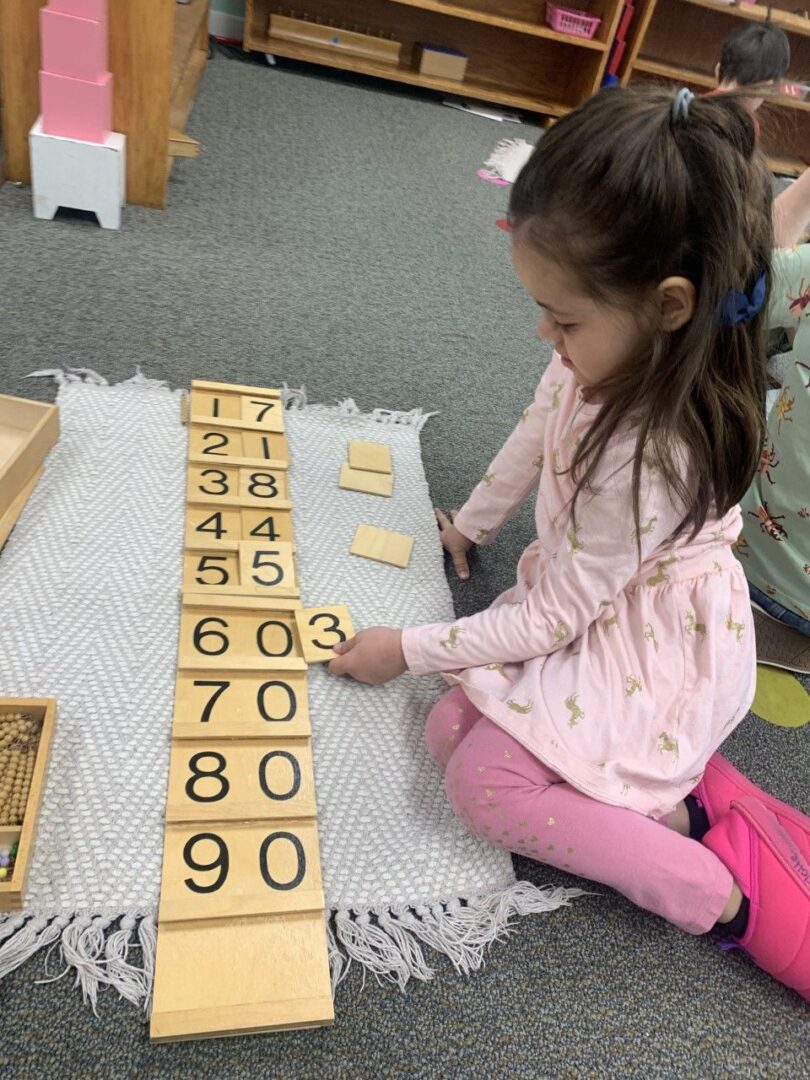 A little girl is playing with numbers on the floor.